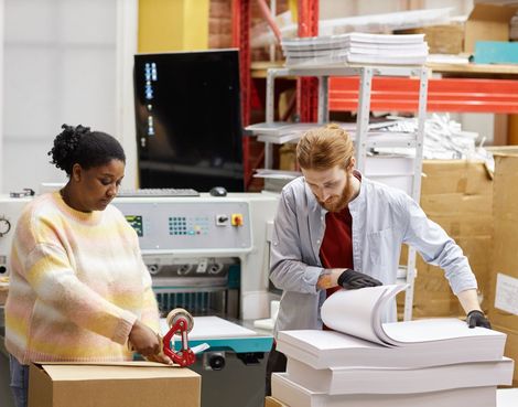 Two print workers reviewing sheets and preparing printed materials at a worktable